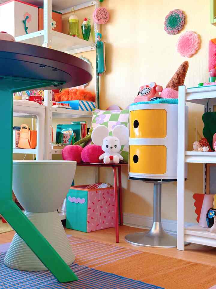 A mid-century modern workspace with yellow walls featuring cute character plushies and colorful decor accents creating a lively atmosphere
