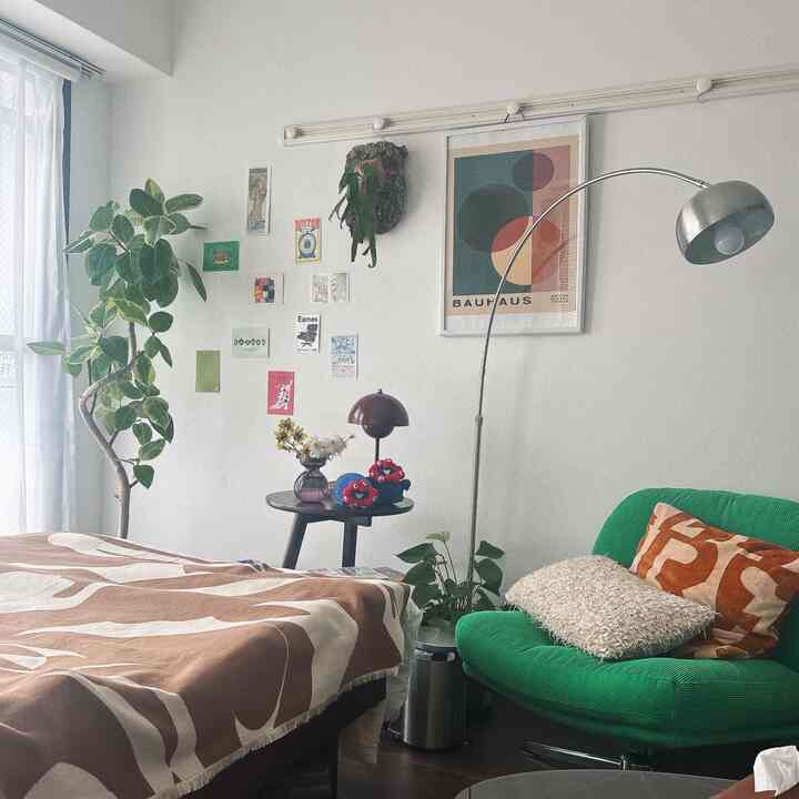 ナチュラルカラーの8畳寝室、大きな植物と緑のアームチェア、茶色の柄の寝具が調和した雰囲気のある空間