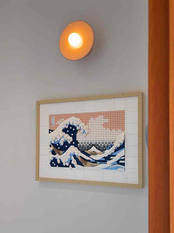 Minimal entrance space with white walls, plate-shaped wall sconce, and LEGO artwork of The Great Wave