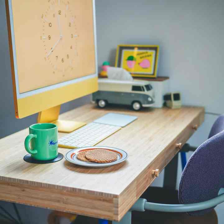 明るい黄色と自然な木目調のワークスペース、デスクには緑色のマグカップとストロープワッフルが置かれた、落ち着いた雰囲気のあるインテリア