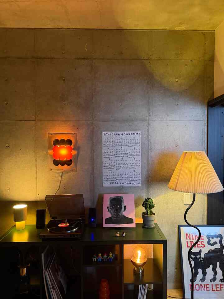 暖かい照明とコンクリートの壁が調和した1LDKのリビングコーナー、レコードプレーヤーとかわいい小物で雰囲気のあるインテリア