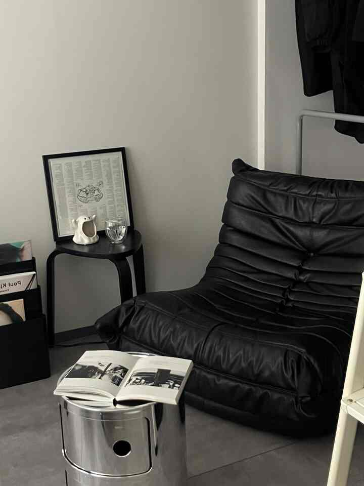 Monotone small living room featuring a black leather sofa and metallic stool with minimalist design