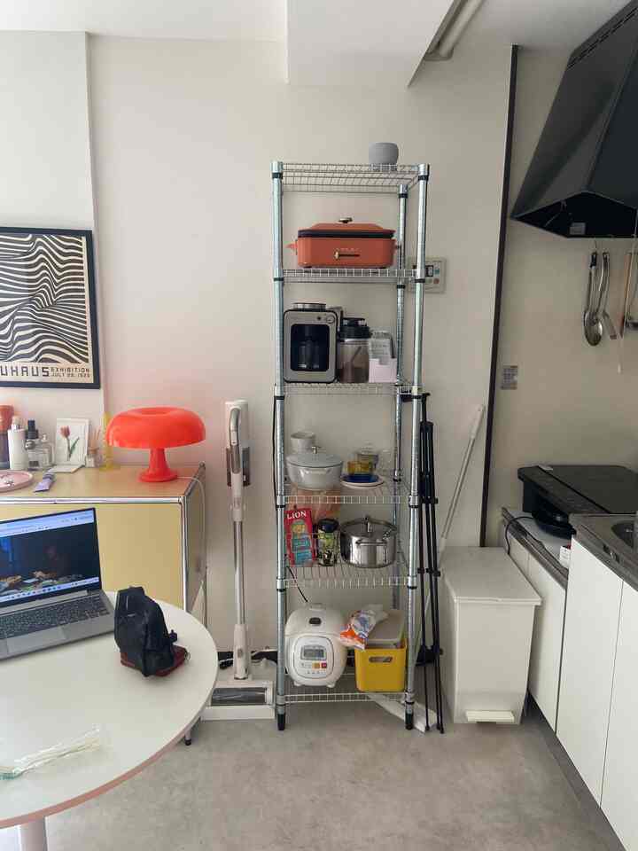 白を基調とした1DKキッチン、メタルシェルフと赤いテーブルランプが配置された雰囲気のあるモダンな空間