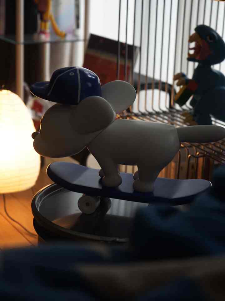 落ち着いた色調のワンルームリビング、青いスケートボードに乗る白い犬のソフビやモンスターのフィギュア、イサム・ノグチのフロアランプが配置されたモダンな雰囲気のインテリア