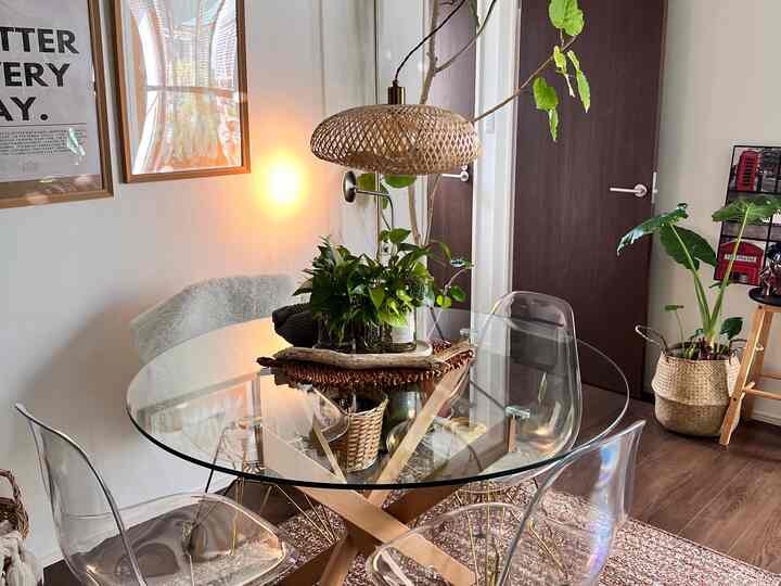 ブラウンの床と木製ドアが調和するダイニング、透明なチェアと円形のガラステーブル、植物が配置されたナチュラルで雰囲気のあるインテリア