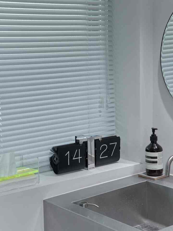 Natural-toned white kitchen space featuring a flip clock on the windowsill and soap dispenser near stainless steel sink, clean and minimal