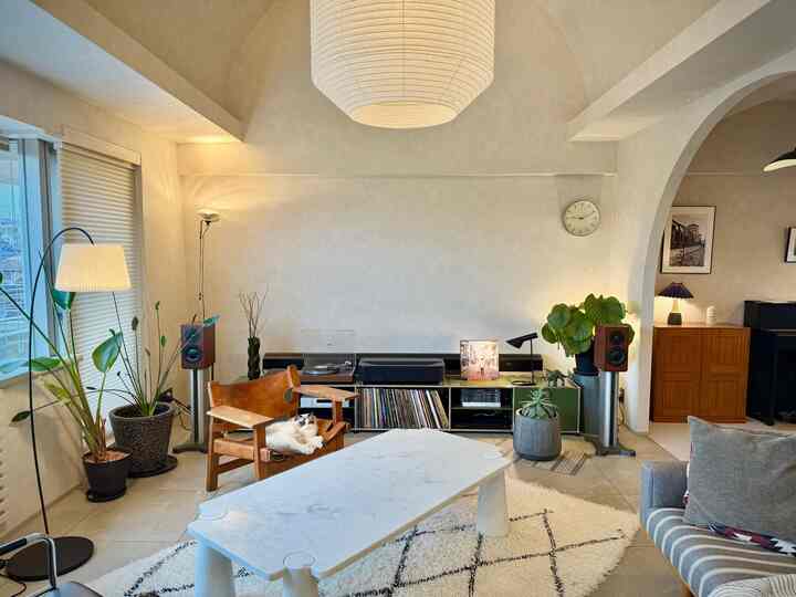 ナチュラルな色調のリビング、マーブルのコーヒーテーブルと猫のいる木製チェアが配置された落ち着いた空間