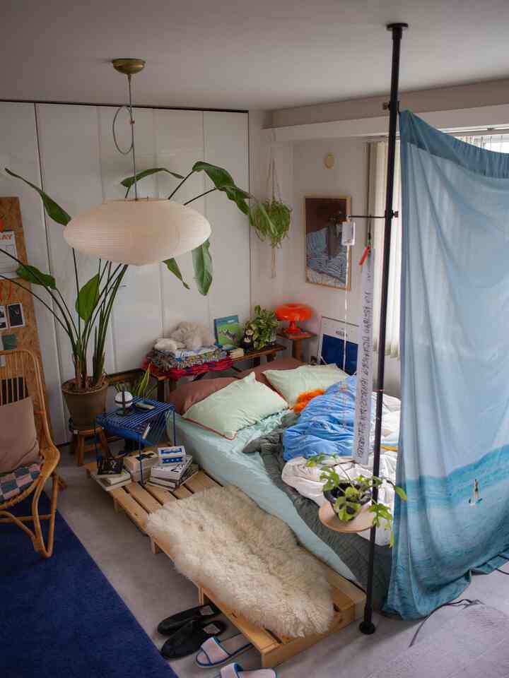 ナチュラルでブルーを基調とした1LDKの寝室、低い木製ベッドと植物が配置された雰囲気のある空間