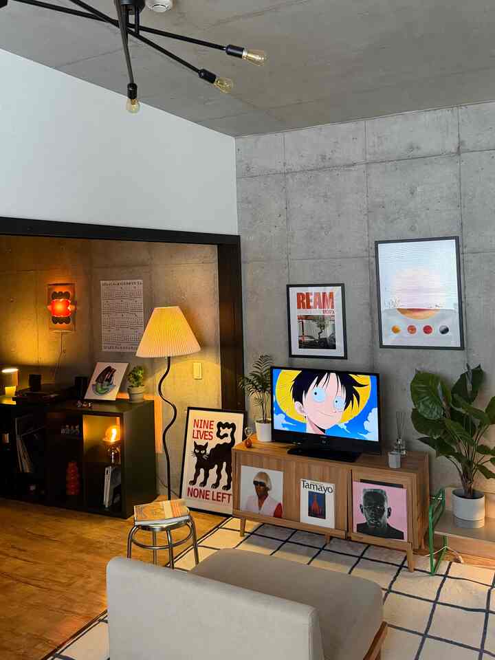 グレーのコンクリート壁とナチュラルな木目調フローリングの1LDKリビング、フロアランプやテレビ台、植物が配置された雰囲気のあるインテリア