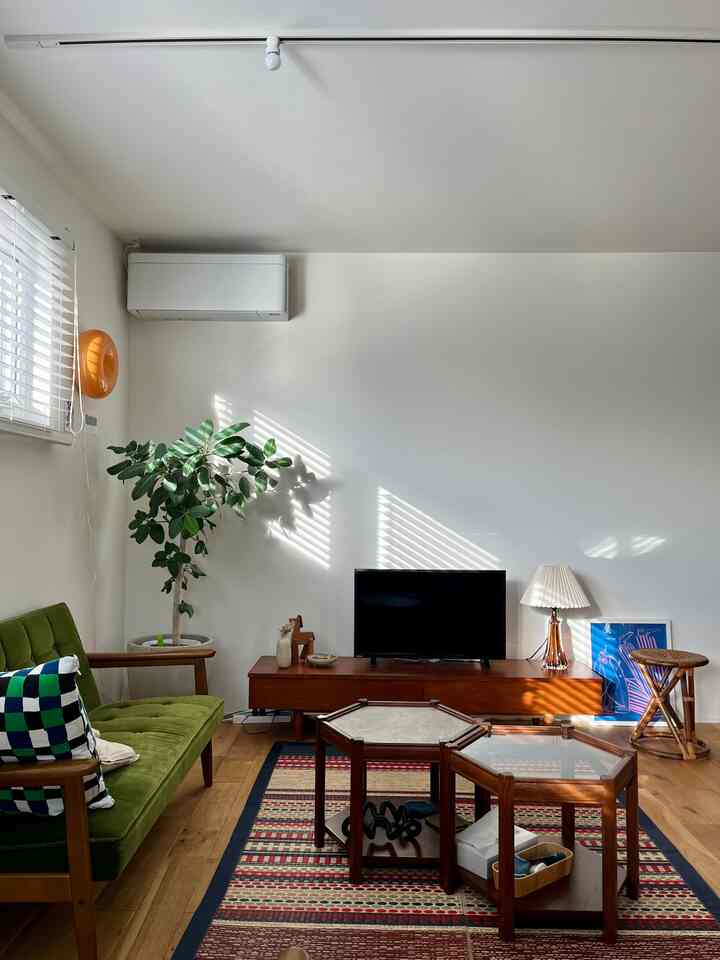 白とブラウンの木目調が調和したリビング、ミッドセンチュリーモダンスタイルの緑色のソファとヴィンテージ家具が配置された温かみのある雰囲気の空間