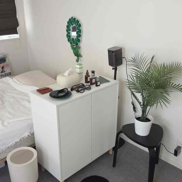 白と緑の色調が映える寝室、植物とスツール、収納キャビネットが配置された雰囲気のあるインテリア