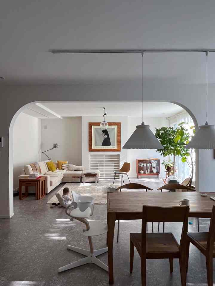 White walls and natural brown furniture in a long and narrow living and dining space featuring a baby and greenery, creating a cozy atmosphere