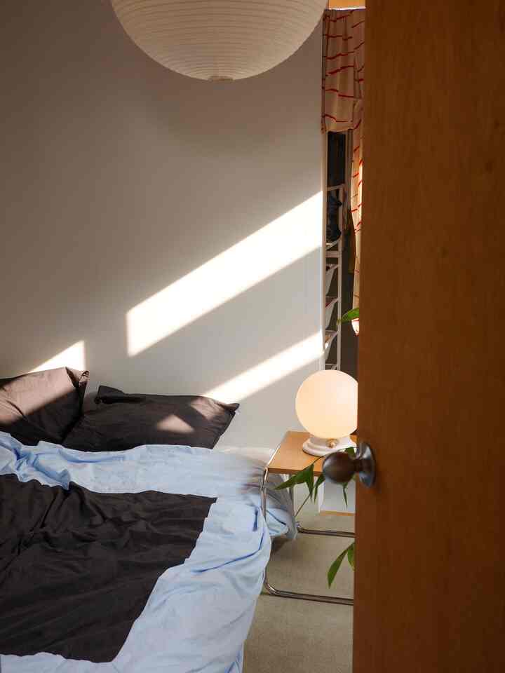 柔らかな白とブラウンの色調の寝室、ブルーとダークブラウンの掛け布団カバーとベージュのカーペットが配置された落ち着いた空間