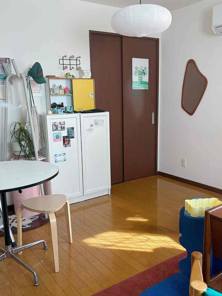 A living room with white and brown tones featuring a round table, stool, and a wall mirror creating a cozy atmosphere