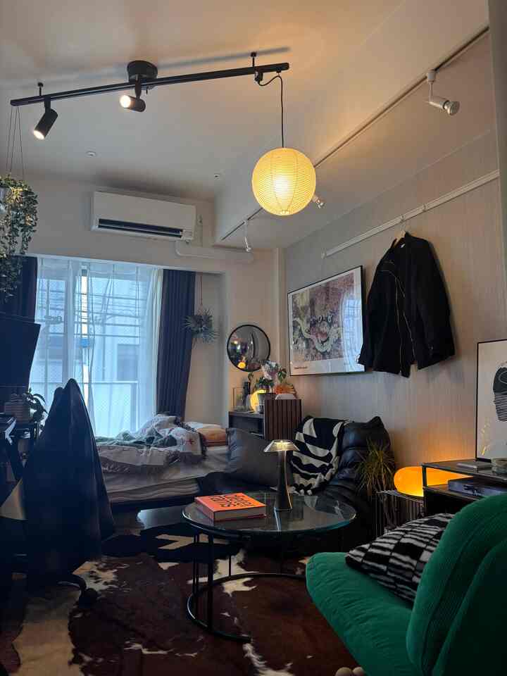 ナチュラルトーンの8畳ワンルームホームオフィス、温かみのある間接照明と黒いソファ、円形のガラステーブルが配置された印象的な空間