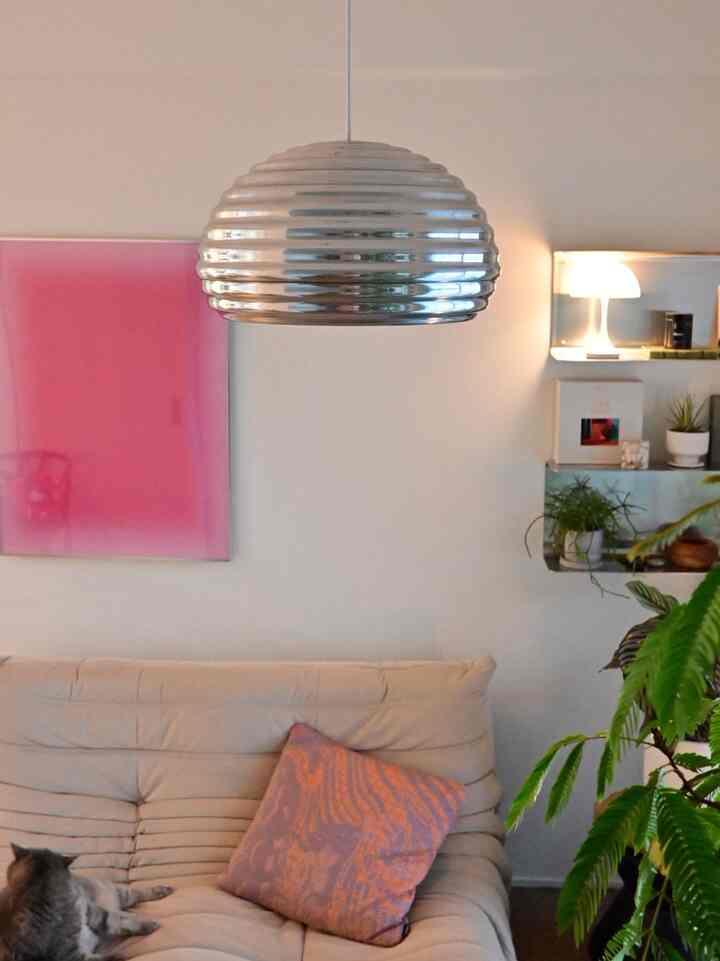 Bright living room with white walls and beige sofa, featuring a silver pendant light, pink poster and cushion as focal natural accents