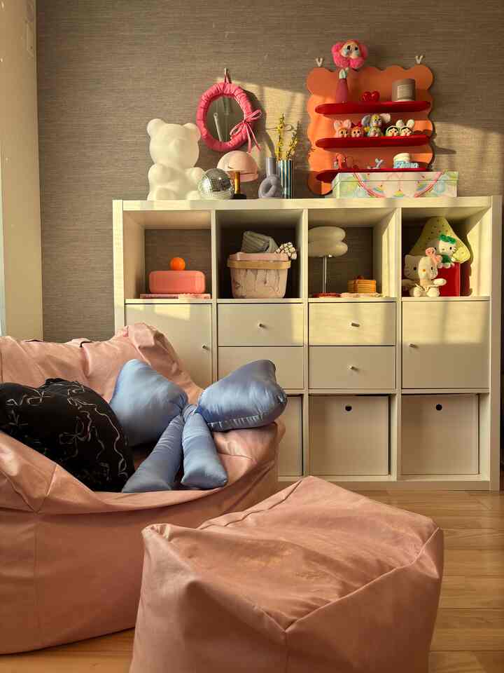 ピンクと白の色調の子供部屋、ビーズクッションソファとおもちゃが並ぶホワイトのKALLAX棚が配置された雰囲気のあるインテリア