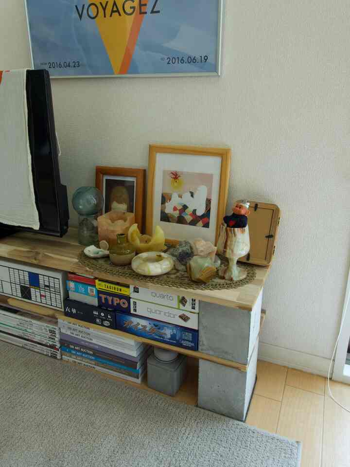 ナチュラルな木目調とコンクリートブロックのミッドセンチュリーモダンなリビングの一角、テレビ台と多様な装飾オブジェが配置された印象的な空間