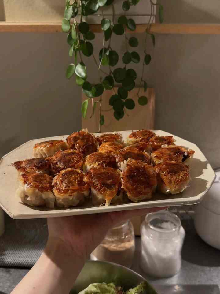 ナチュラルな色調のキッチン、手に持ったお皿にきれいに並べられたこんがり焼けた餃子が配置された印象的な空間