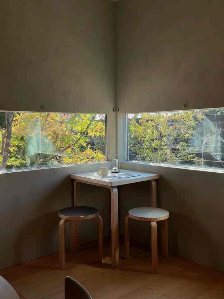 Natural toned compact corner space with wooden stools and white dining table by windows, featuring a USB portable lamp creating a cozy atmosphere