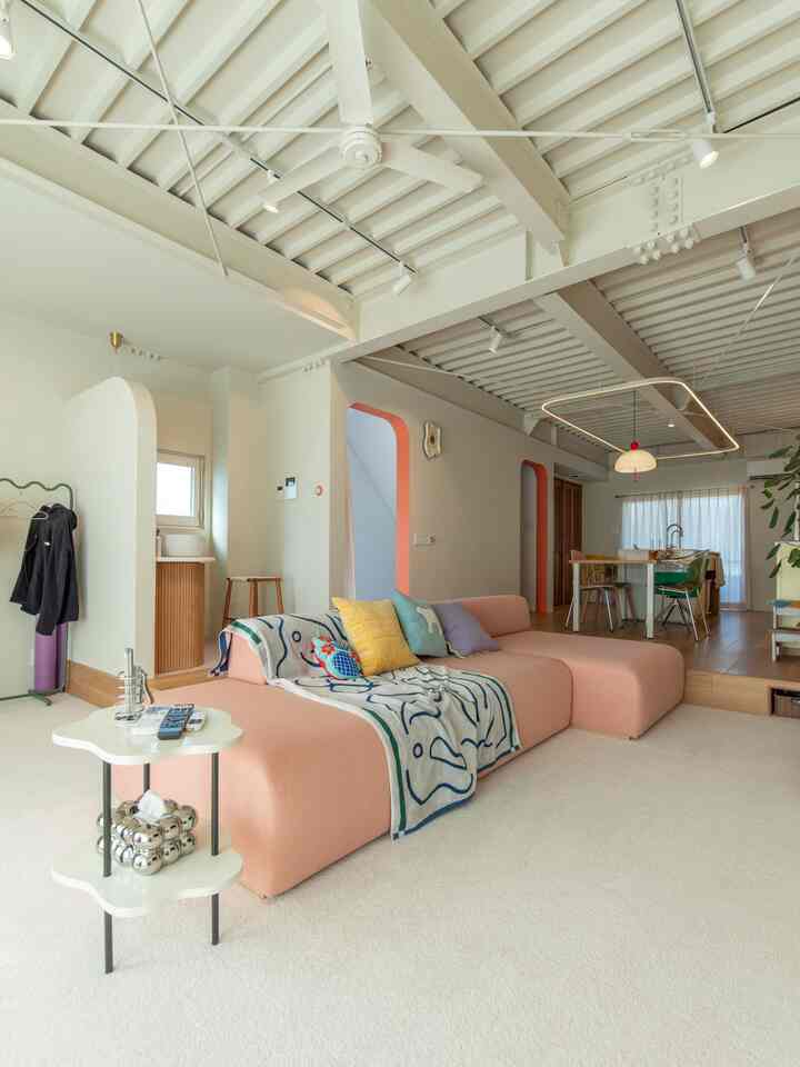 Bright natural-toned living room with a pink sofa and colorful cushions arranged on an ivory carpet creating a cozy space