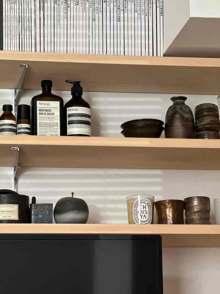 ナチュラルな色調の1LDKの一人暮らしリビング、木製の棚にディフューザーやキャンドル、オブジェが整然と置かれた雰囲気のあるインテリア