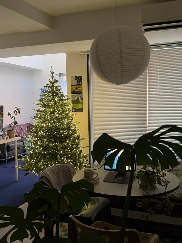 White and navy toned living room with a decorated Christmas tree, plants, round dining table, and a pendant light creating a cozy atmosphere