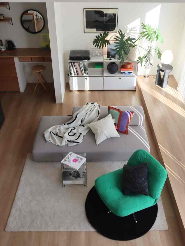 白い壁とナチュラルな木の床が調和したモダンなリビング、緑色のアームチェアとストライプのスローがアクセントの空間