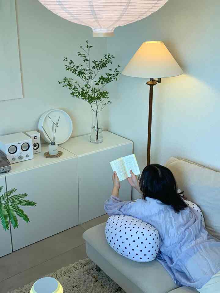 ナチュラルな色調のリビング、ベージュのソファと白い水玉クッション、植物とフロアランプが配置された温かみのある雰囲気のインテリア