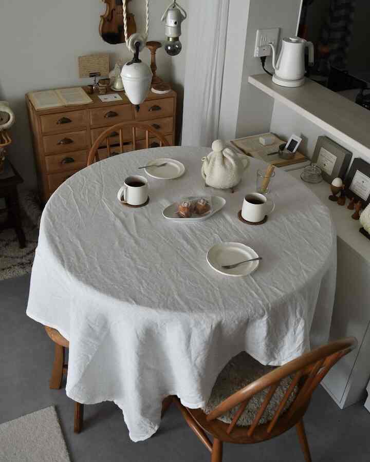 ホワイトとブラウンの色調のキッチン・ダイニング、丸テーブルにテーブルクロスと食器が配置された雰囲気のあるインテリア