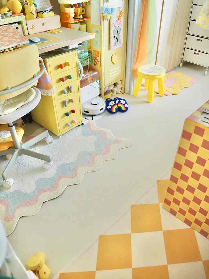 黄色とアイボリーの色調の子供部屋、デスクとスツール、多彩なラグが配置された温かみのあるシンプルなインテリア