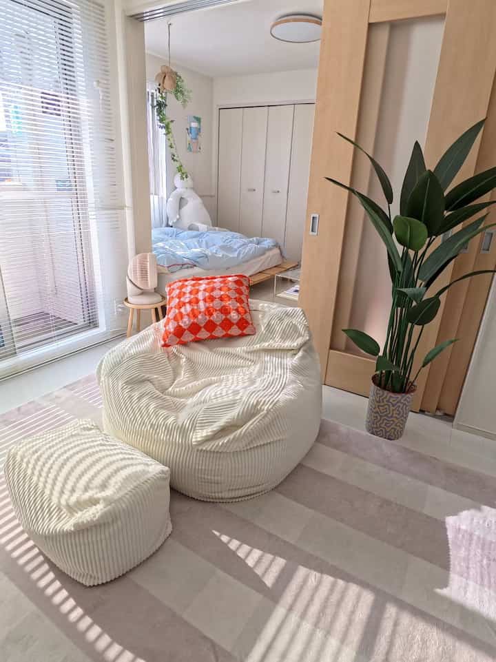 Beige and white toned compact bedroom featuring a large bean bag and indoor plant, creating a cozy atmosphere