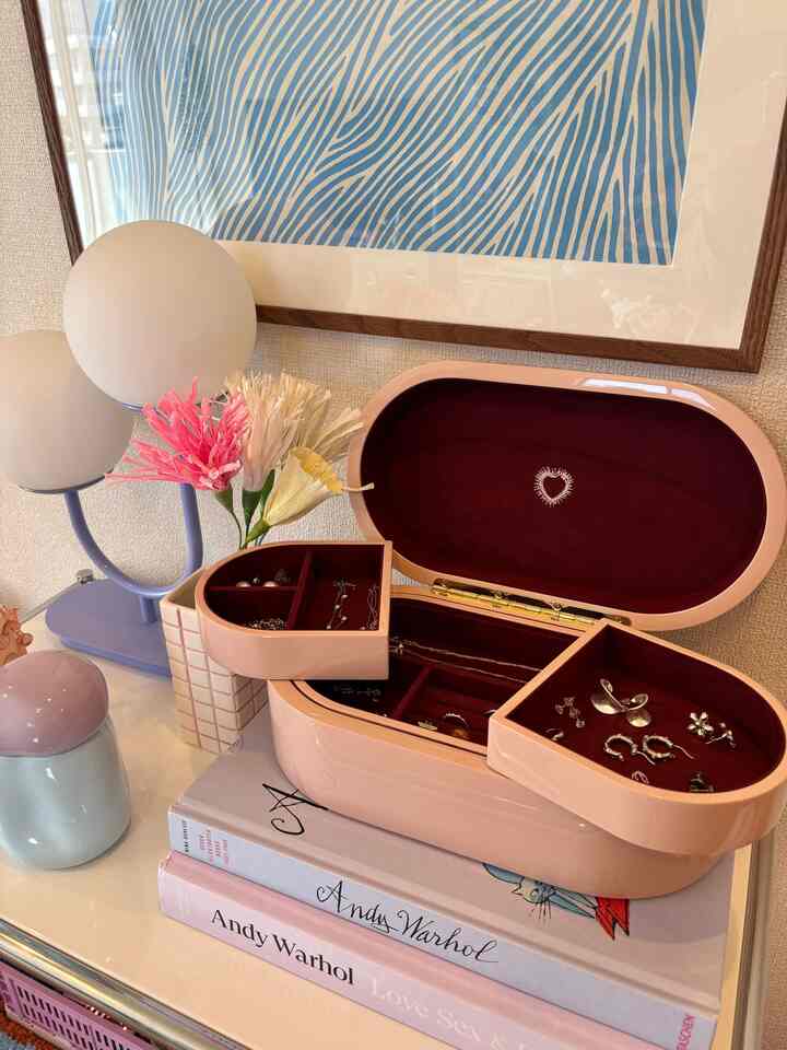 ピンクのジュエリーボックスが置かれたモダンでシンプルなインテリア、青い抽象画と丸いテーブルランプが配置された空間