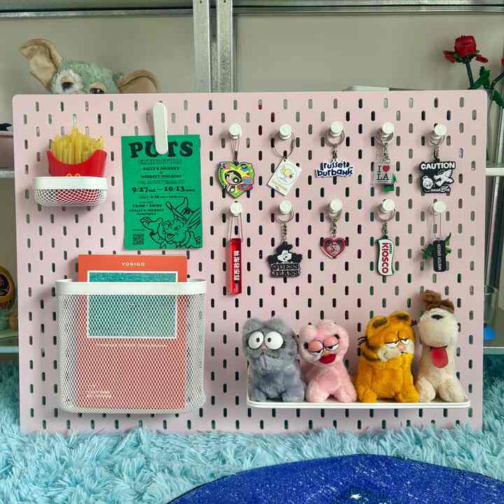 Light pink pegboard featuring colorful keychains and plush cat figurines arranged neatly, creating a cozy storage idea space