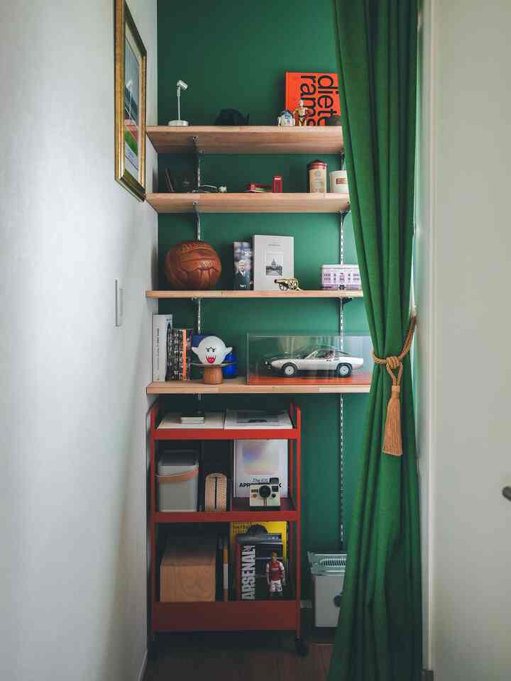 深い緑色の壁とカーテンが印象的な書斎、イケアのニッサフォースワゴンと多様な飾りが配置された空間