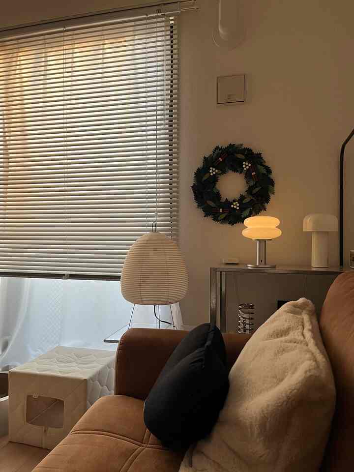 暖かいブラウンとホワイトのトーンの1LDKリビング、クリスマスリースと間接照明が配置された雰囲気のあるインテリア