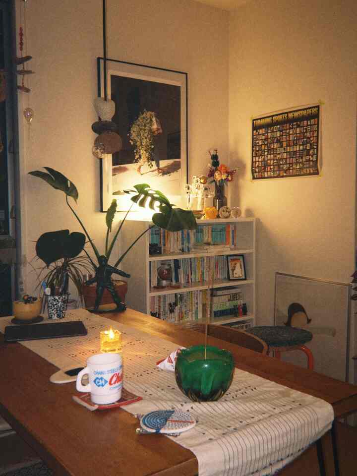 温かみのある木目調と緑の植物が融合したミッドセンチュリーモダンのダイニング、キャンドルと個性的な額縁が配置された雰囲気のあるインテリア