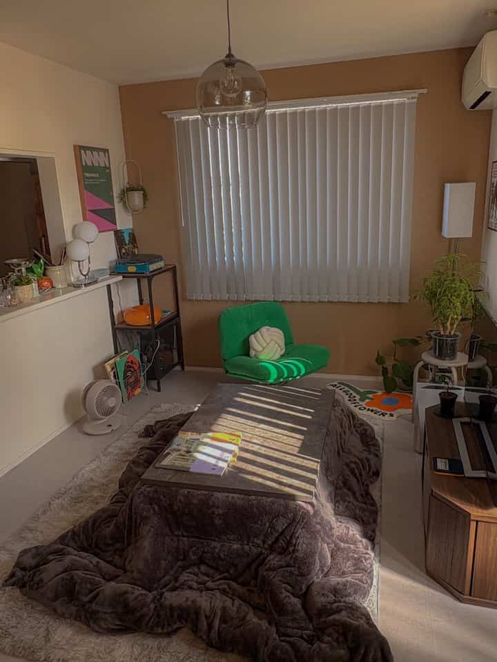 Living room with light brown walls and green armchair, central kotatsu table and shaggy rug create a cozy atmosphere