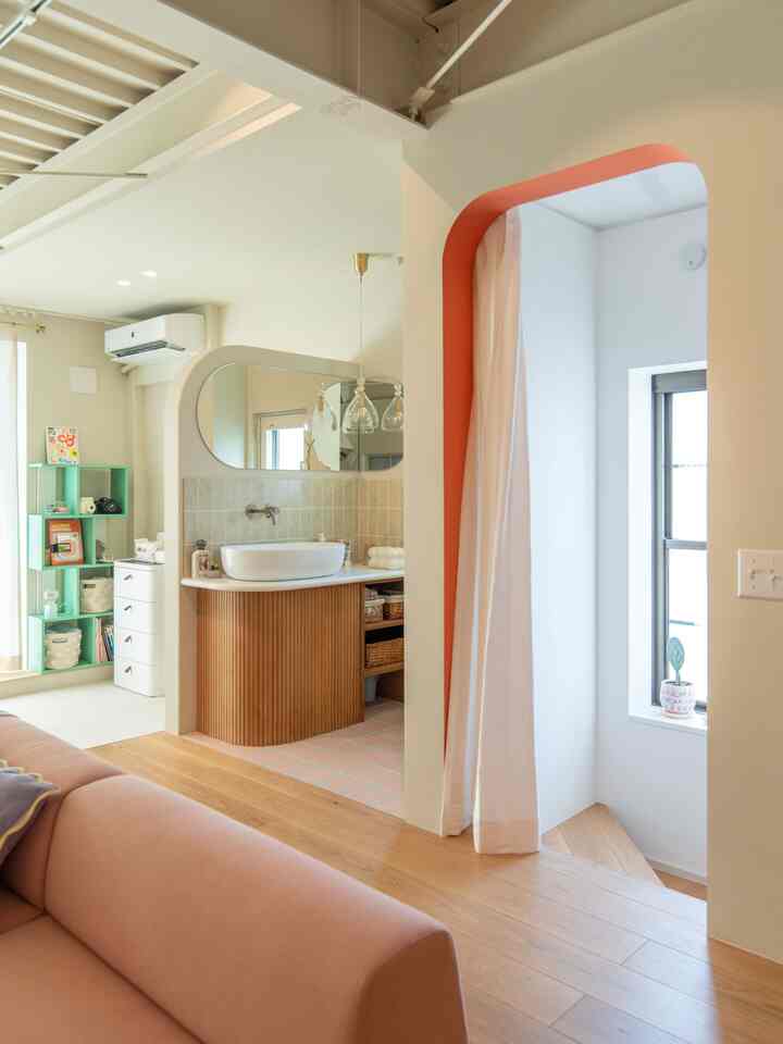 ナチュラルな色調のリビングと繋がる洗面台、木目調のフローリングとピンクのソファが調和した印象的な空間