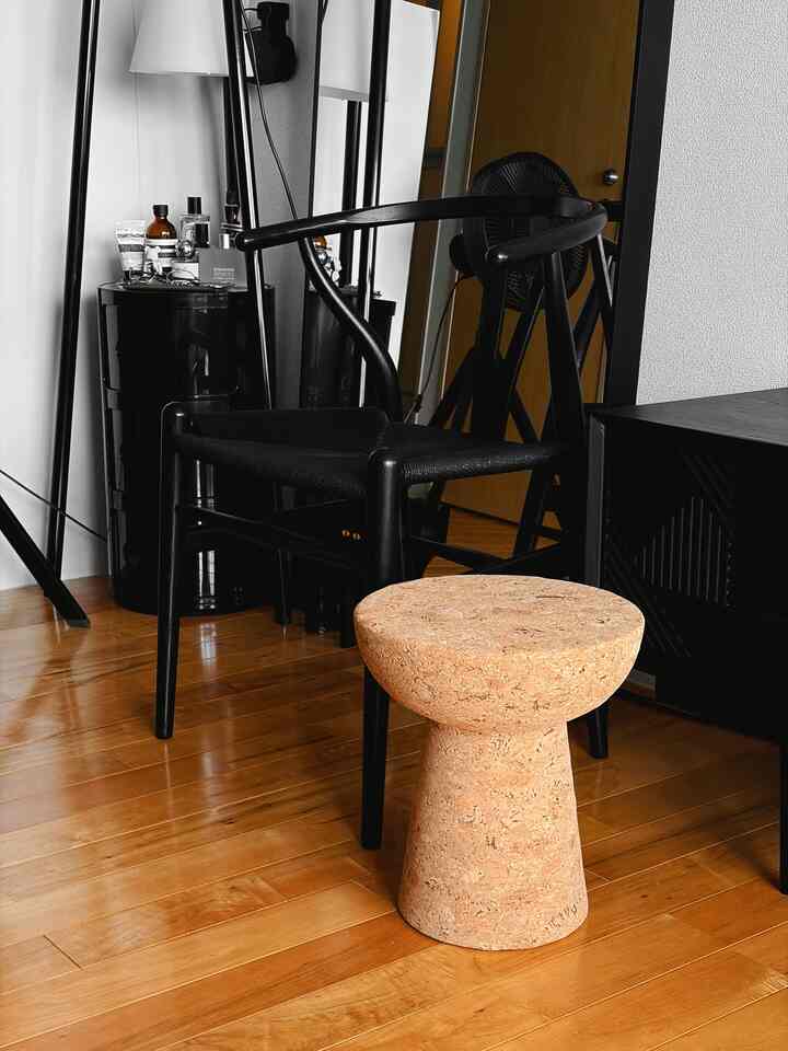 Modern studio apartment with black furniture and cork stool on natural wood-toned floor