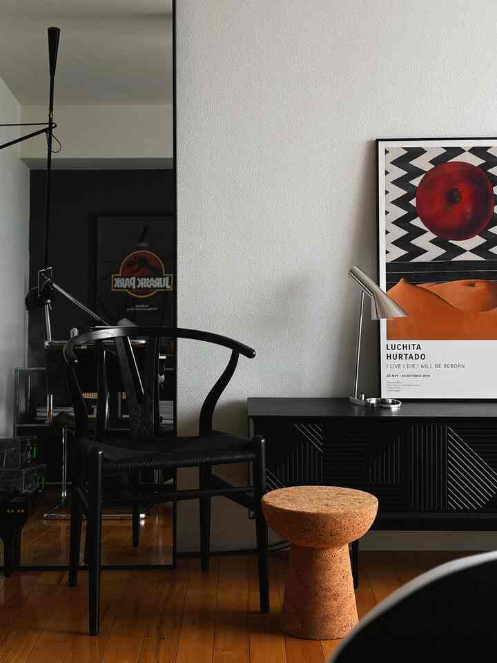 ブラックとウッドトーンの家具が調和したリビング、大きな鏡とデザイナーチェア、サイドボードが配置された雰囲気あるインテリア