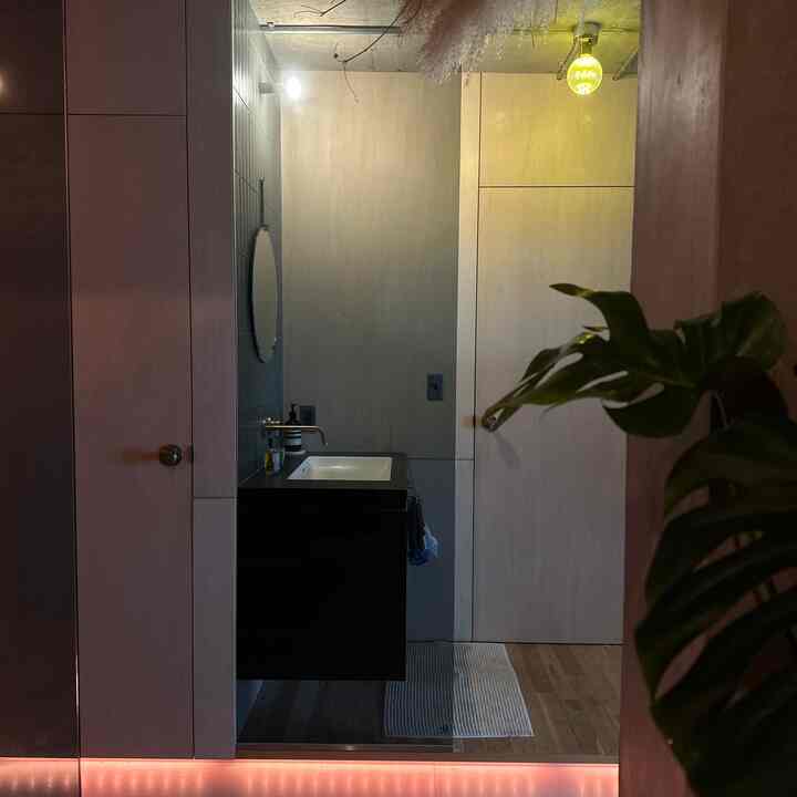 ウッドトーンとブラックが調和するバスルーム、洗面台と丸い鏡、バスマットが配置された落ち着いた空間