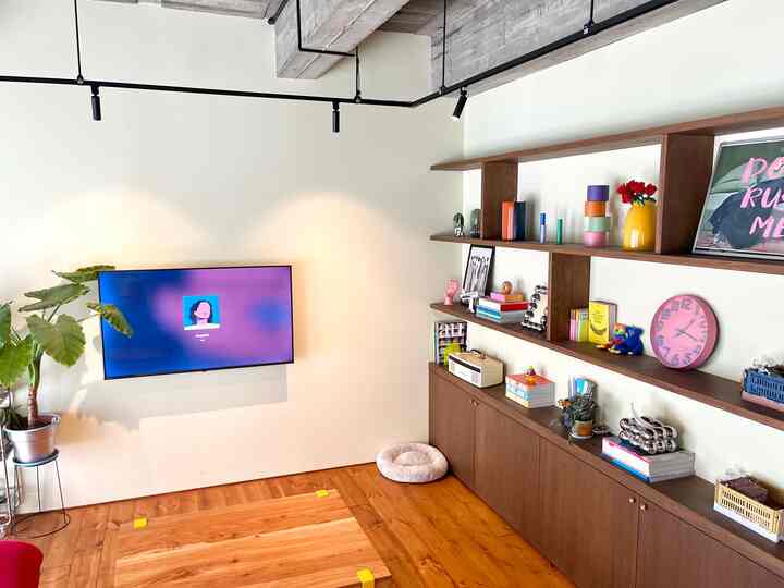 A living room with white walls and wood-toned floor and shelves, featuring a wall-mounted TV and a pet bed for a cozy atmosphere