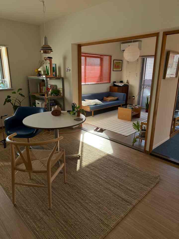 オレンジ色のブラインドとブルーのミッドセンチュリーソファが配置された温かみのあるリビングとダイニングの空間