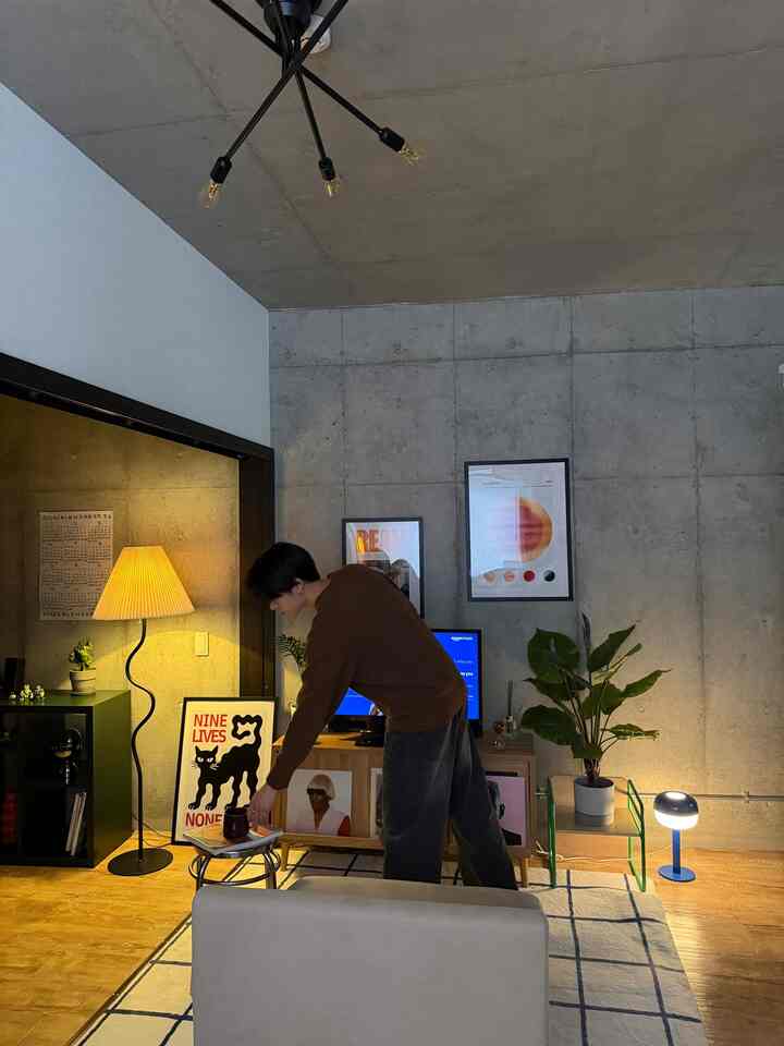 落ち着いたナチュラルトーンの1LDK無機質空間、コンクリート壁とスツール、フロアランプが調和するインテリア