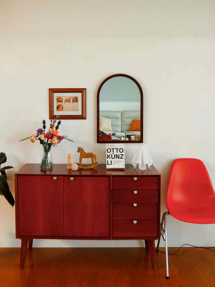 ブラウンの木目調キャビネットとオレンジ色の椅子が配置されたホワイト壁の北欧風の雰囲気あるインテリア