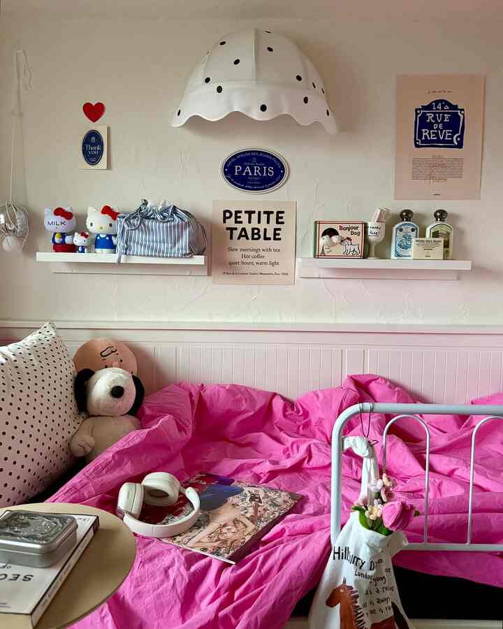 ピンクの寝具と白い壁、フレンチ風のポスターがある居心地の良い寝室
