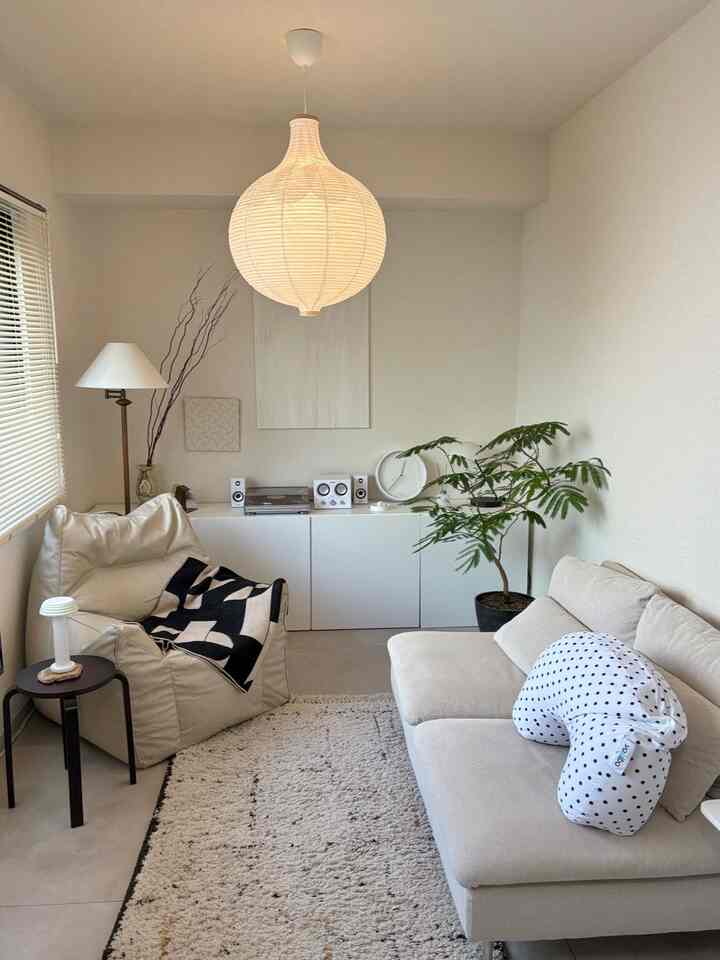 ベージュ調のリビング、ベージュのソファとビーンバッグチェア、ペンダントライトと植物が配置された落ち着いた空間