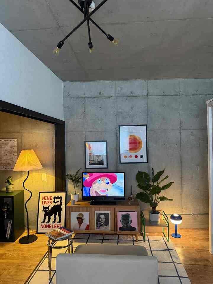 ナチュラルな色調とモダンなインダストリアルなコンクリート壁が調和するリビング、テレビ台やフロアランプ、植物が配置された印象的な空間
