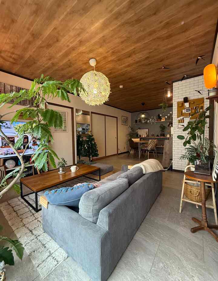 ナチュラルな木目調の天井とグレーのソファが配されたリビング、植物とテーブルが置かれた雰囲気のあるインテリア